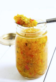 a glass jar filled with food sitting on top of a white wooden table next to a spoon