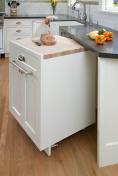 a white kitchen with black counter tops and an island in front of the sink that has a loaf of bread on it