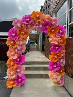 an arch made out of paper flowers on the side of a building with steps leading up to it