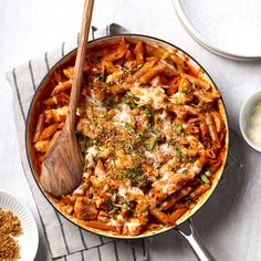 a skillet filled with pasta and sauce next to two plates of breadcrumbs