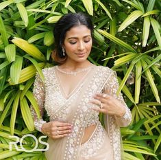 a woman in a sheer dress standing next to some plants and greenery with her hands on her hips