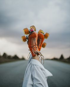 someone is holding up their skates in the air on an empty road with clouds overhead