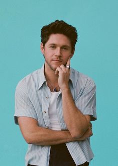 a man with his hand on his chin posing for a photo against a blue background