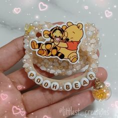 a person holding a winnie the pooh brooch with pearls and beads on it