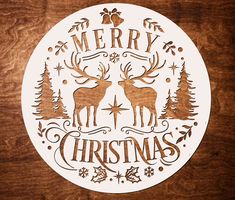 a merry christmas sticker with deer and pine trees in the center on a wooden surface