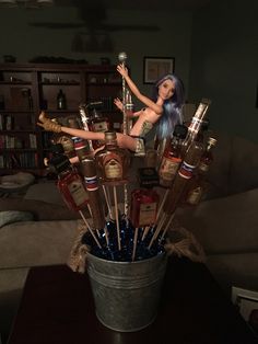 a woman with blue hair is sitting in a bucket filled with liquor bottles and miniature dolls