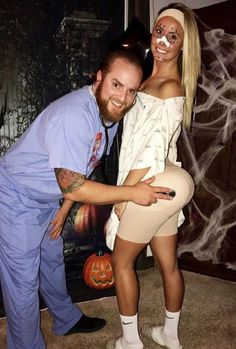 a man and woman posing for a photo in front of a halloween poster with ghost makeup on