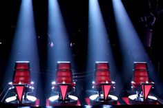 four red chairs sitting on top of a stage with spotlights shining in the background