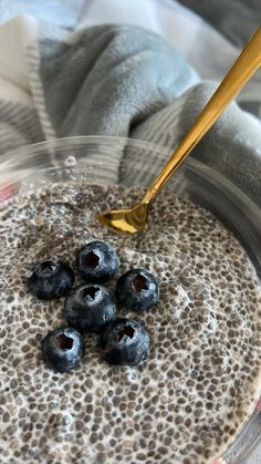 blueberries in a glass bowl being stirred with a spoon by someone's hand