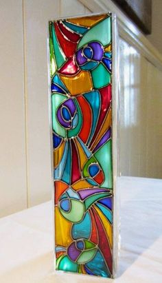 a colorful glass vase sitting on top of a white table next to a window sill