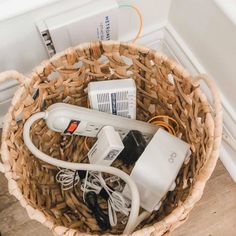 a basket filled with different types of electronic devices and cords on top of a wooden floor