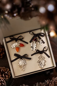 four christmas ornaments in a white box on a table with pine cones and other decorations