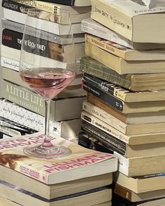 a glass of wine sitting on top of a stack of books next to a pile of books