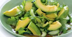 a green plate filled with sliced avocado and cilantro sauce on top of lettuce