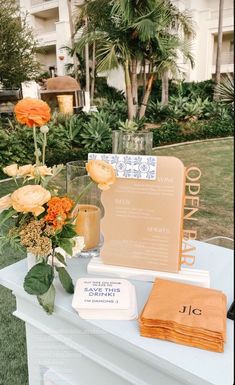 an orange flower arrangement on top of a table next to a menu and napkins