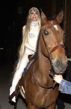 a woman riding on the back of a brown horse next to a man in white