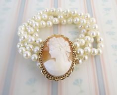 "This Vintage Victorian revival 14k gold pearl bracelet has a wonderful carved shell cameo. The cameo carving depicts a young lady facing left with an elaborate bow in her hair and draped clothing. It is set in 14 karat gold (tested) with a twisted frame and serves as a box clasp with the end marked, \"14k\". A safety clip closure is in place to better secure the bracelet. There are 4 strands of 5.9mm knotted white pearls with nice luster. The bracelet has an approx. inner circumference of 5 3/4 Elegant Gold Cameo Bracelets, Elegant Cameo Bracelet Gift, Elegant Cameo Wedding Bracelets, Elegant Wedding Cameo Bracelets, Elegant Cameo Bracelet Jewelry, Elegant Cameo Bracelet For Formal Occasions, Draped Clothing, Gold Pearl Bracelet, Victorian Revival