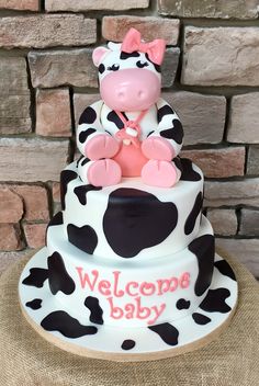 a baby cow sitting on top of a white and black cake with pink lettering that says welcome baby