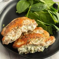 two pieces of chicken on a black plate with spinach leaves next to it and a fork