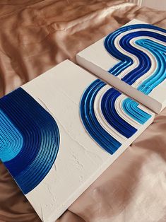 two blue and white abstract paintings on a bed