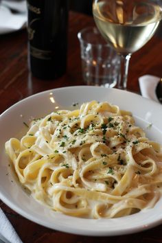 a white plate topped with pasta next to a glass of wine