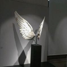 a sculpture of two wings on top of a black pedestal in front of a white wall