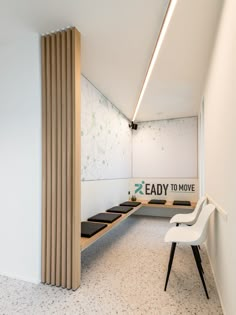 an empty waiting room with white chairs and wood slats on the wall, in front of a sign that reads eady to move