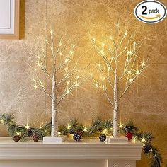 three small trees with pine cones and lights in front of a fireplace