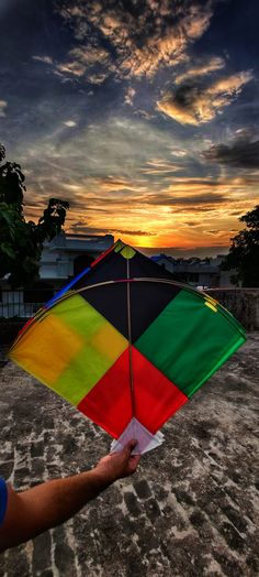 a person holding a colorful kite in front of a cloudy sky at sunset or dawn