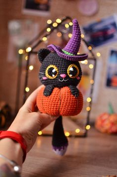 a crocheted black cat sitting on top of an orange pumpkin wearing a witches hat