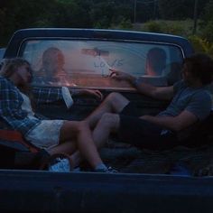 two people sitting in the back of a pick up truck with a screen on it