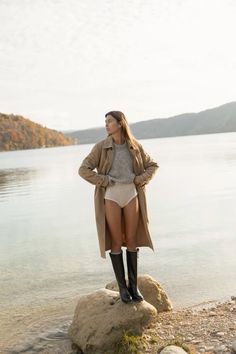 a woman standing on top of a rock next to the ocean wearing short shorts and boots