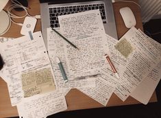 a laptop computer sitting on top of a wooden desk covered in notes and papers next to a mouse