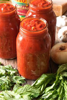 three jars filled with red sauce sitting on top of a wooden table next to vegetables