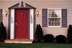 a red door and some bushes in front of a house