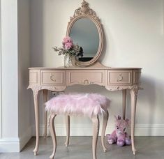 a pink vanity with a mirror, stool and flower vase on the floor next to it