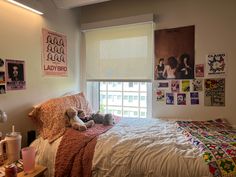 a bedroom with posters on the wall and stuffed animals on the bed in front of the window