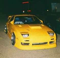 a yellow sports car is parked on the side of the road at night with other cars in the background