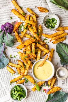 french fries with dipping sauce on newspaper next to greens and dips in small bowls