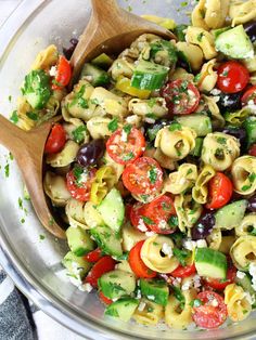 a bowl full of pasta salad with olives, tomatoes and cucumbers in it