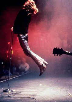 a person jumping in the air on stage with a guitar and microphone to their side