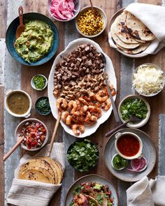 an assortment of food is laid out on a wooden table with bowls and spoons