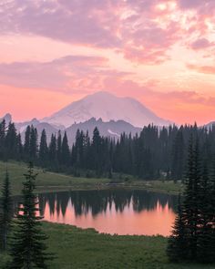 the sun is setting over a mountain range with a lake and pine trees in front of it