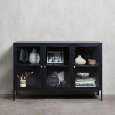 a black cabinet with glass doors and vases on the top shelf next to it