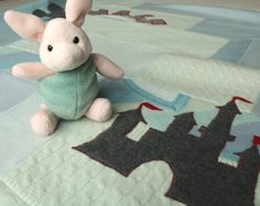 a small stuffed animal sitting on top of a bed next to a quilted bedspread