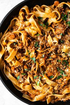 pasta with meat and parsley in a skillet on a white table top, ready to be eaten