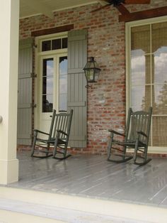 two rocking chairs on the front porch of a brick house with an open door and shutters