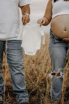 a pregnant woman holding a white shirt while standing next to a man in a field