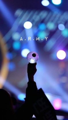 a person holding up a cell phone in front of a stage with the words armmy on it