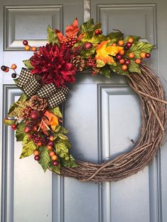 a wreath is hanging on the front door with autumn leaves and pomegranates